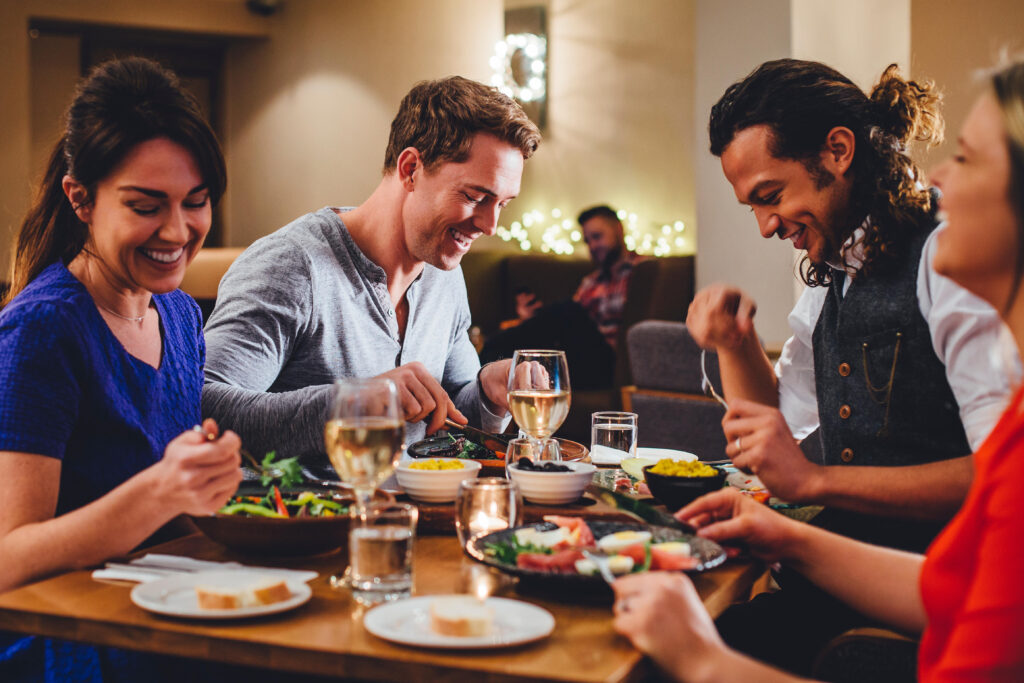 Group of friends dining together as a chef serves a dish. กลุ่มเพื่อนรับประทานอาหารร่วมกันขณะเชฟเสิร์ฟอาหาร