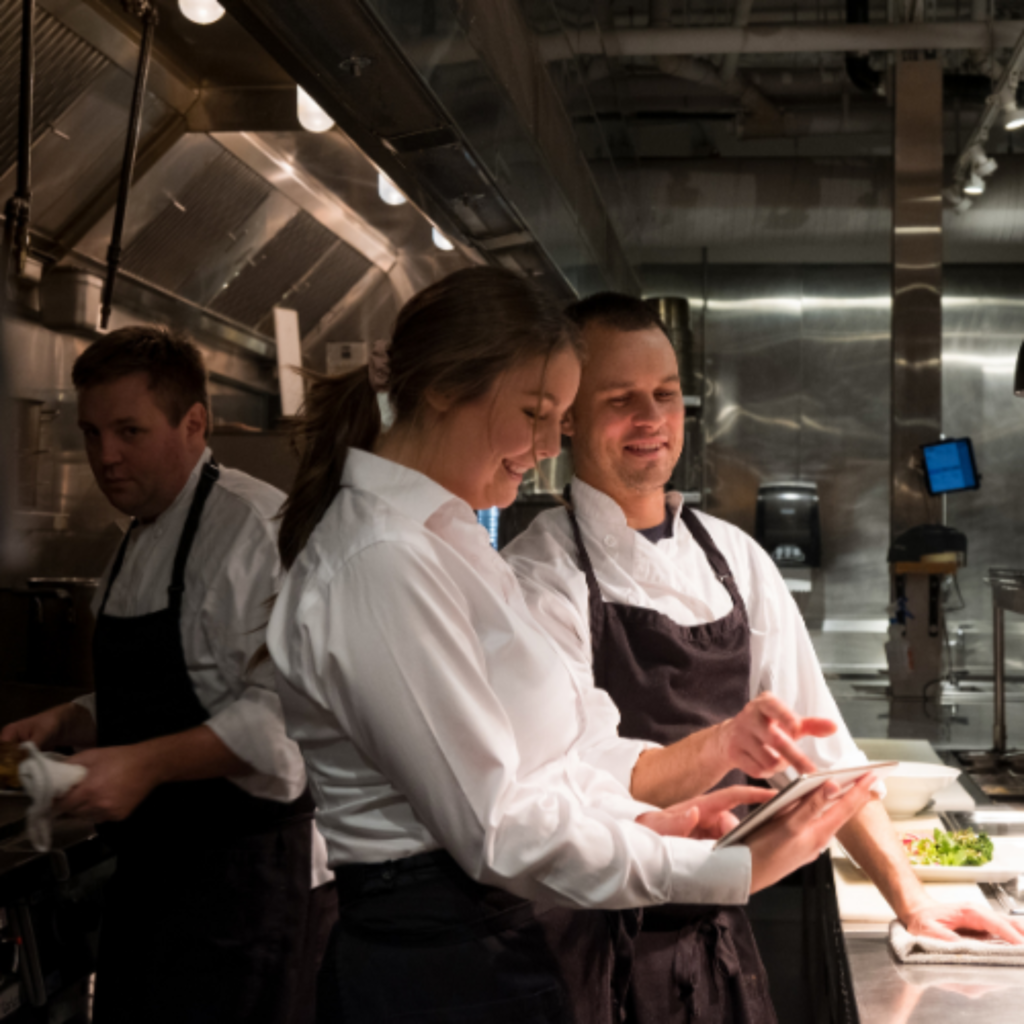Chefs plating dishes at a restaurant kitchen pass. เชฟกำลังจัดจานอาหารที่จุดส่งอาหารในครัว